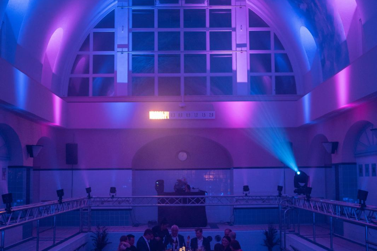Blick in das Hallenbad. Menschen sitzen an der Tafel.